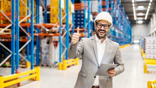 Smiling businessman with hardhat on factory floor giving thumbs up